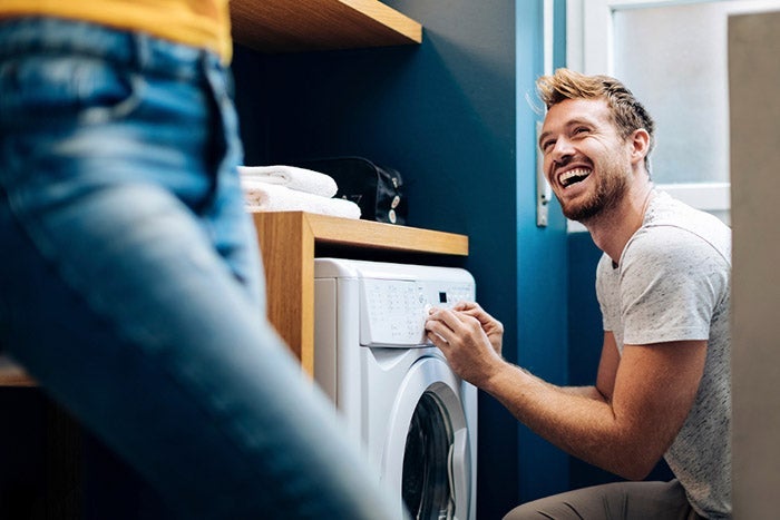 A man in a utility room loading clothes into a washing machine,