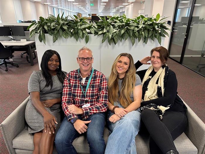 4 people sat on a sofa smiling at getting their photo taken