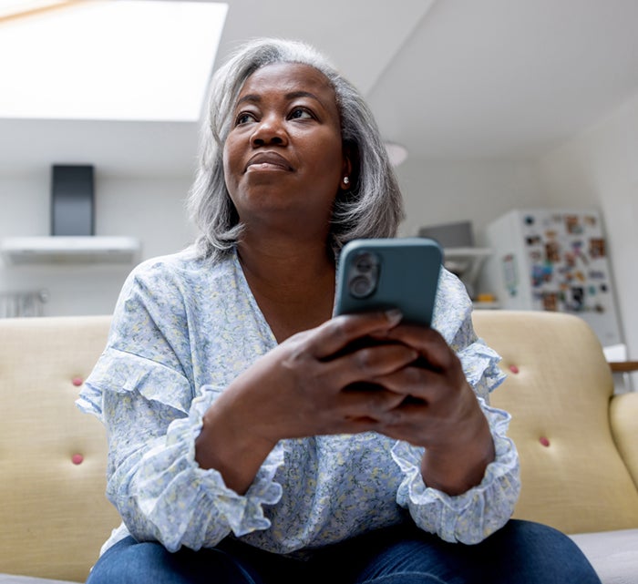 Mature black woman at home texting on her cell phone while sitting on the couch