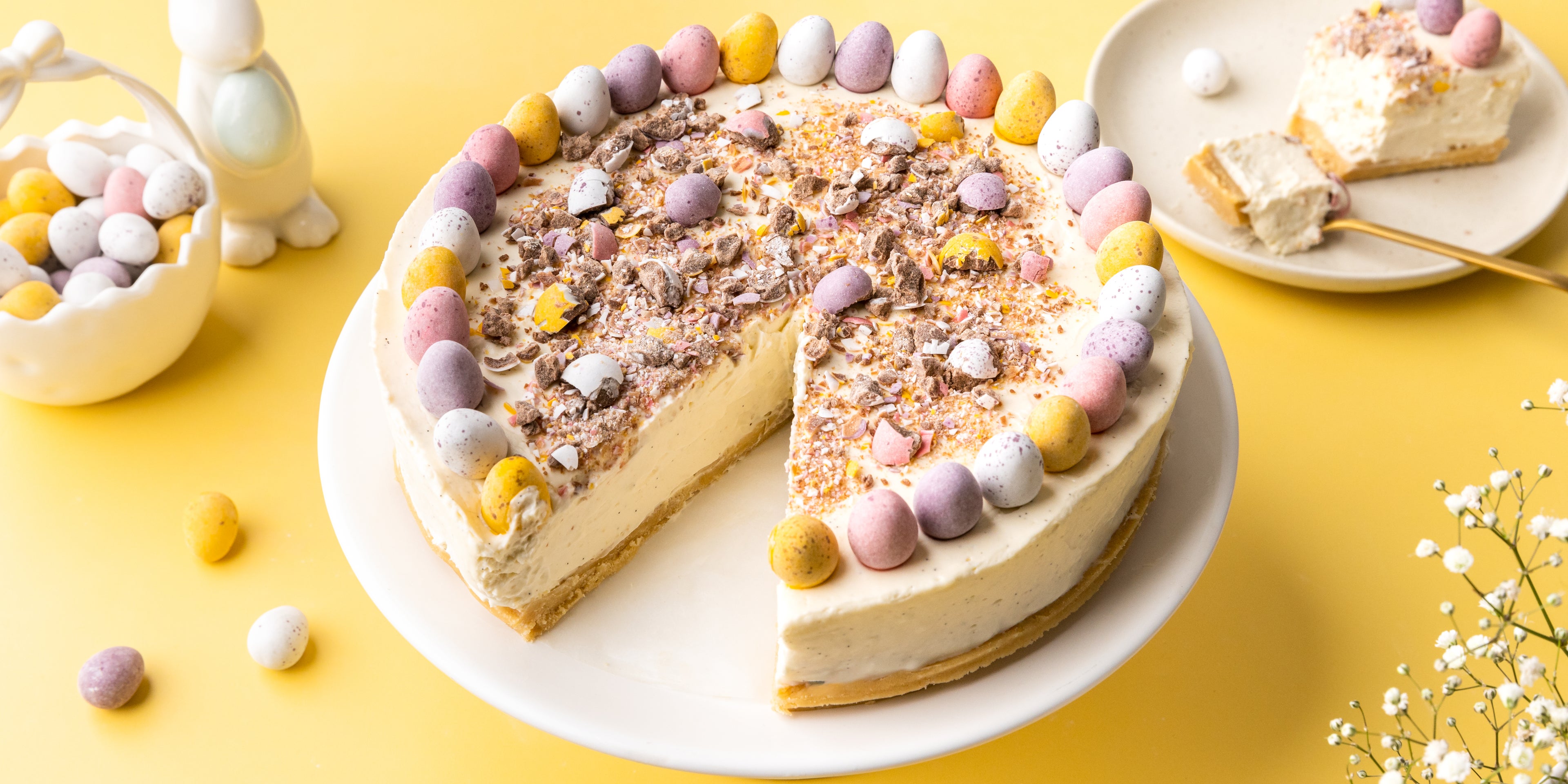 Mini egg cheesecake topped with pastel coloured mini eggs with a slice cut out.