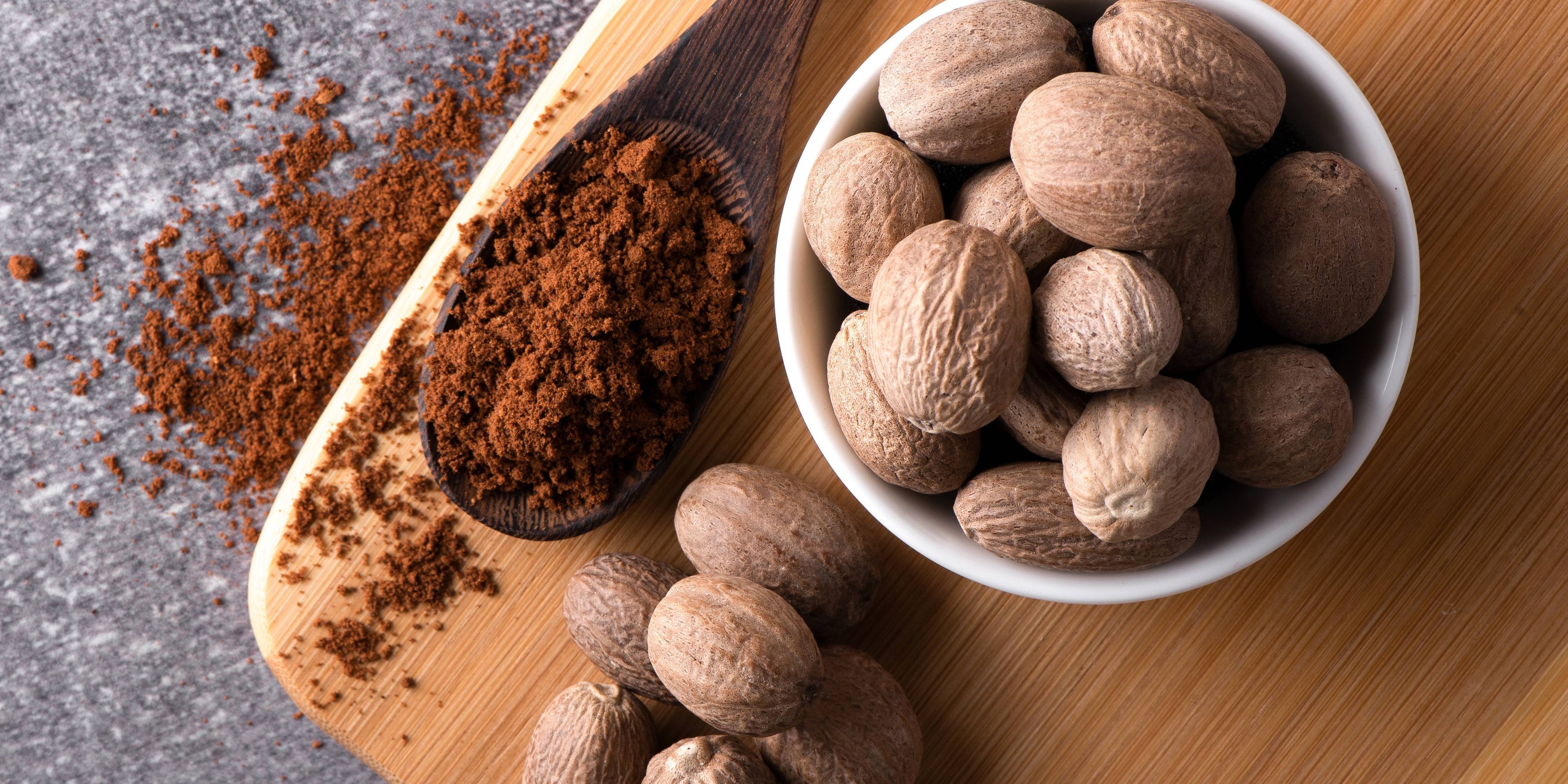Freshly-ground nutmeg in a wooden spoon next to whole nutmegs
