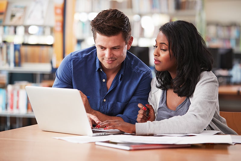 Two students working together on laptop In college library