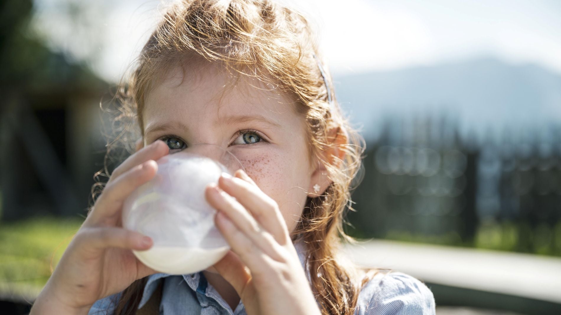 Ein kleines Mädchen mit roten Haaren und Sommersprossen trinkt aus einem Glas Milch.