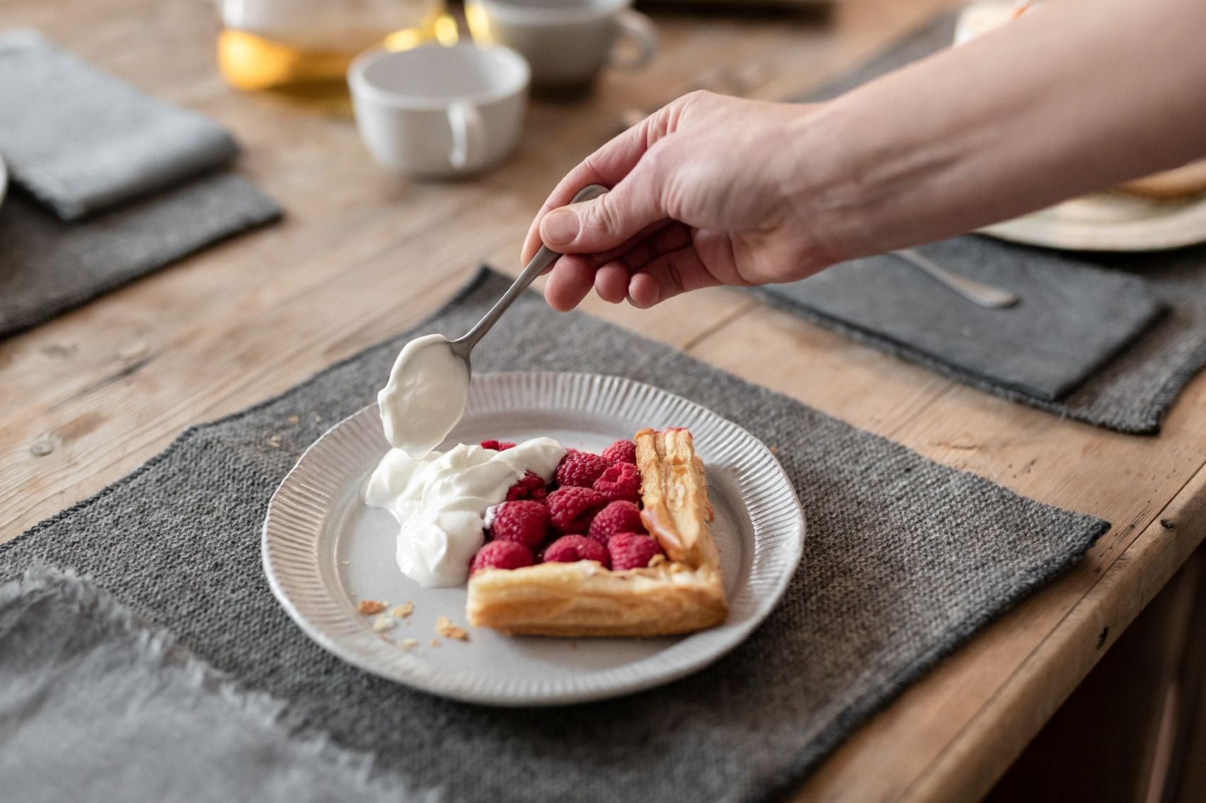 Eine Hand mit einem Löffel gibt Joghurt auf ein Stück Kuchen mit Himbeeren.