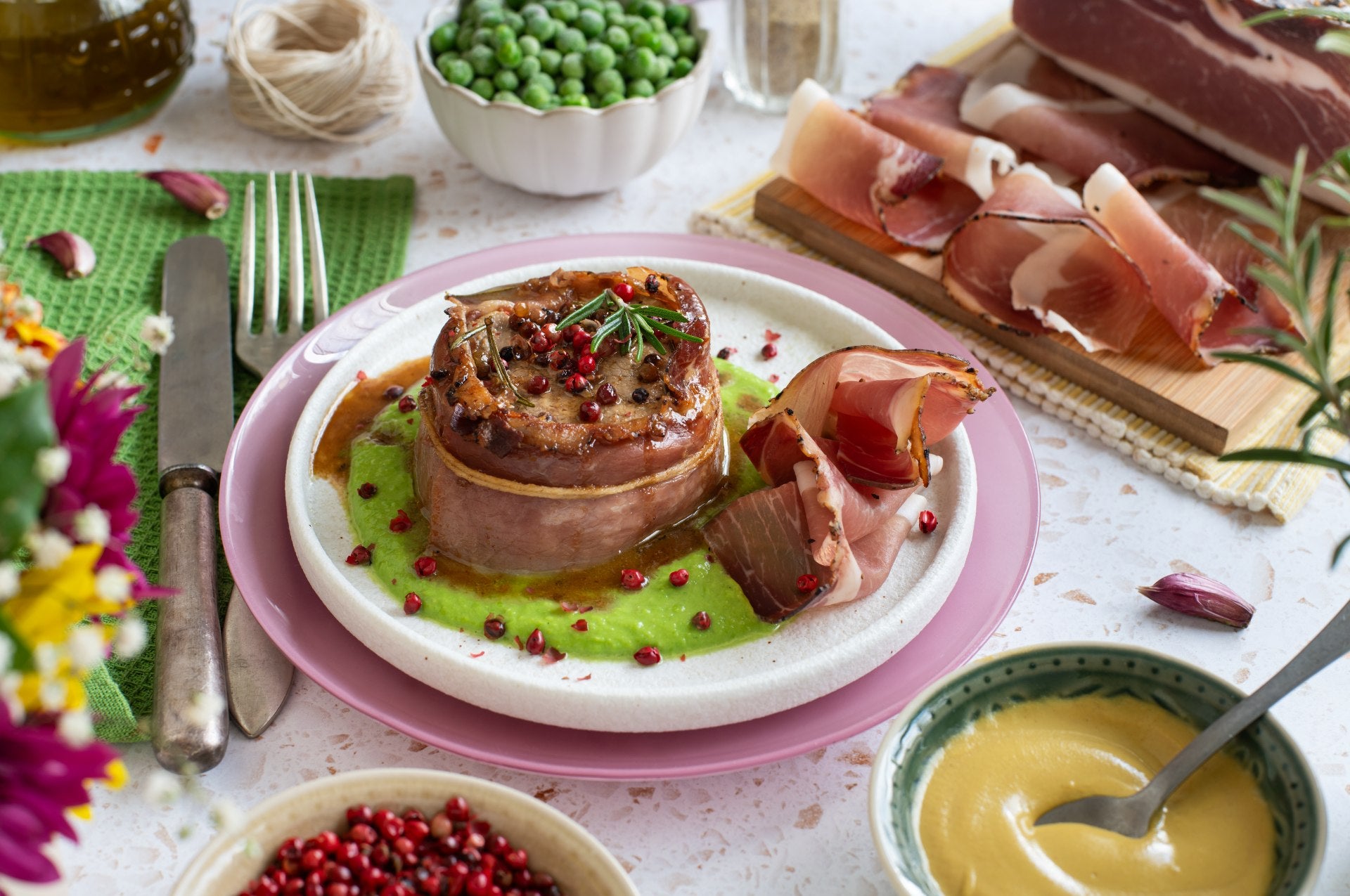 Schweinefilet mit Senf umwickelt in Südtiroler Speck g.g.A., serviert auf einer Erbsencreme mit rosa Pfefferkörnern.