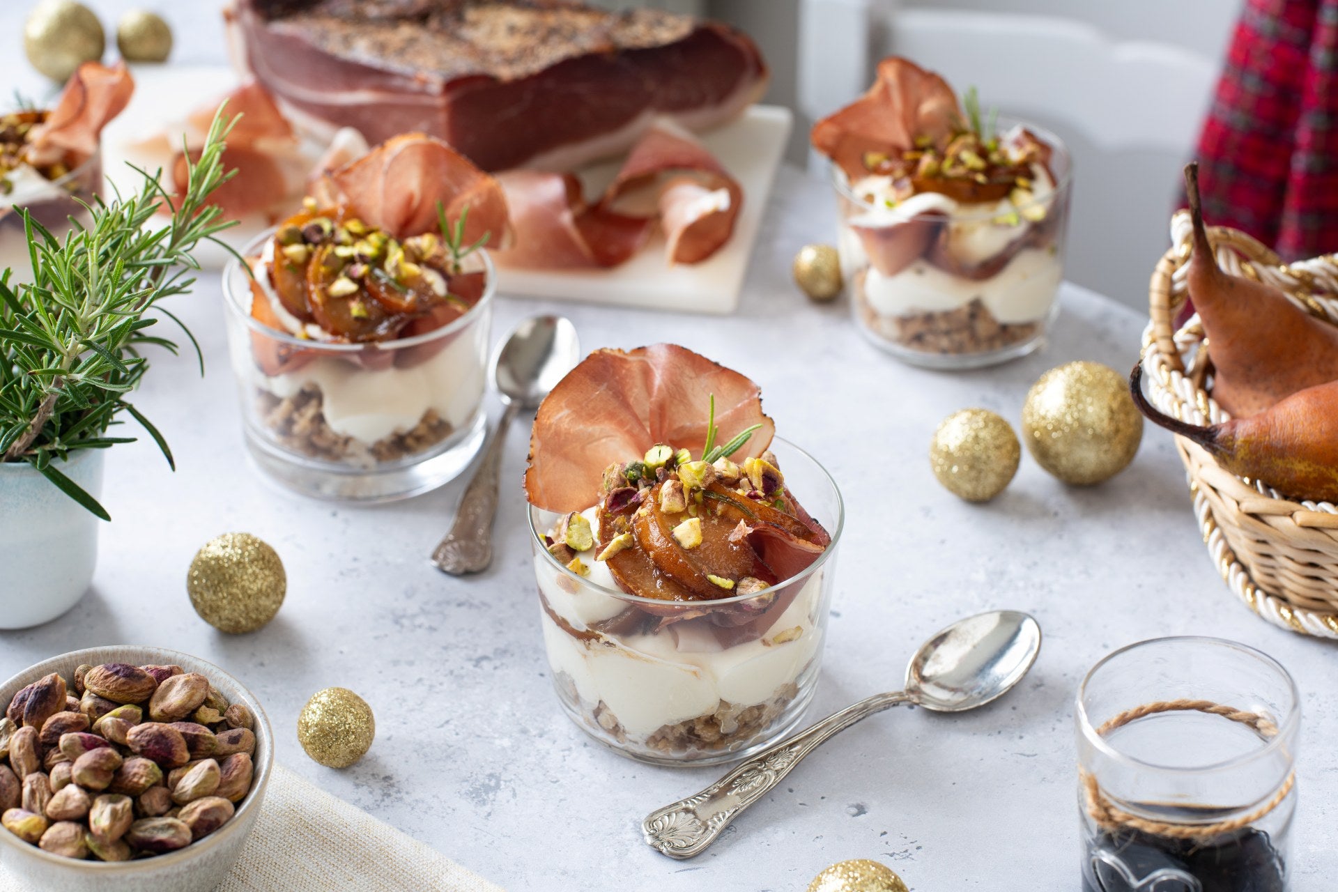 Robiola-Cheesecake mit Balsamicobirnen, Speck Alto Adige g.g.A. und Pistazien, als Dessert im Glas mit festlicher Dekoration serviert.