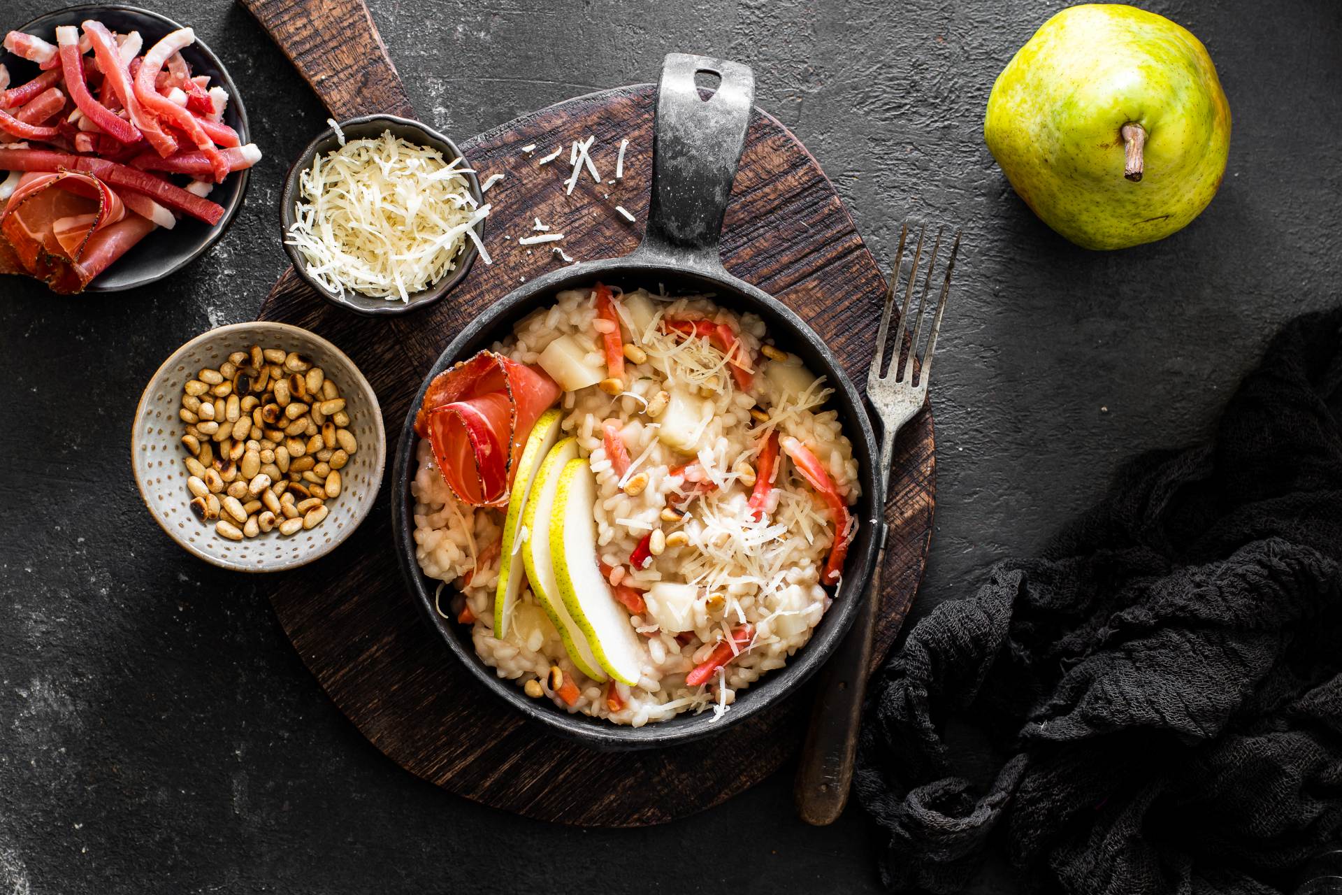 Cremiges Risotto mit Birnenspalten, Südtiroler Speck g.g.A. und geriebenem Käse, in der Pfanne serviert.