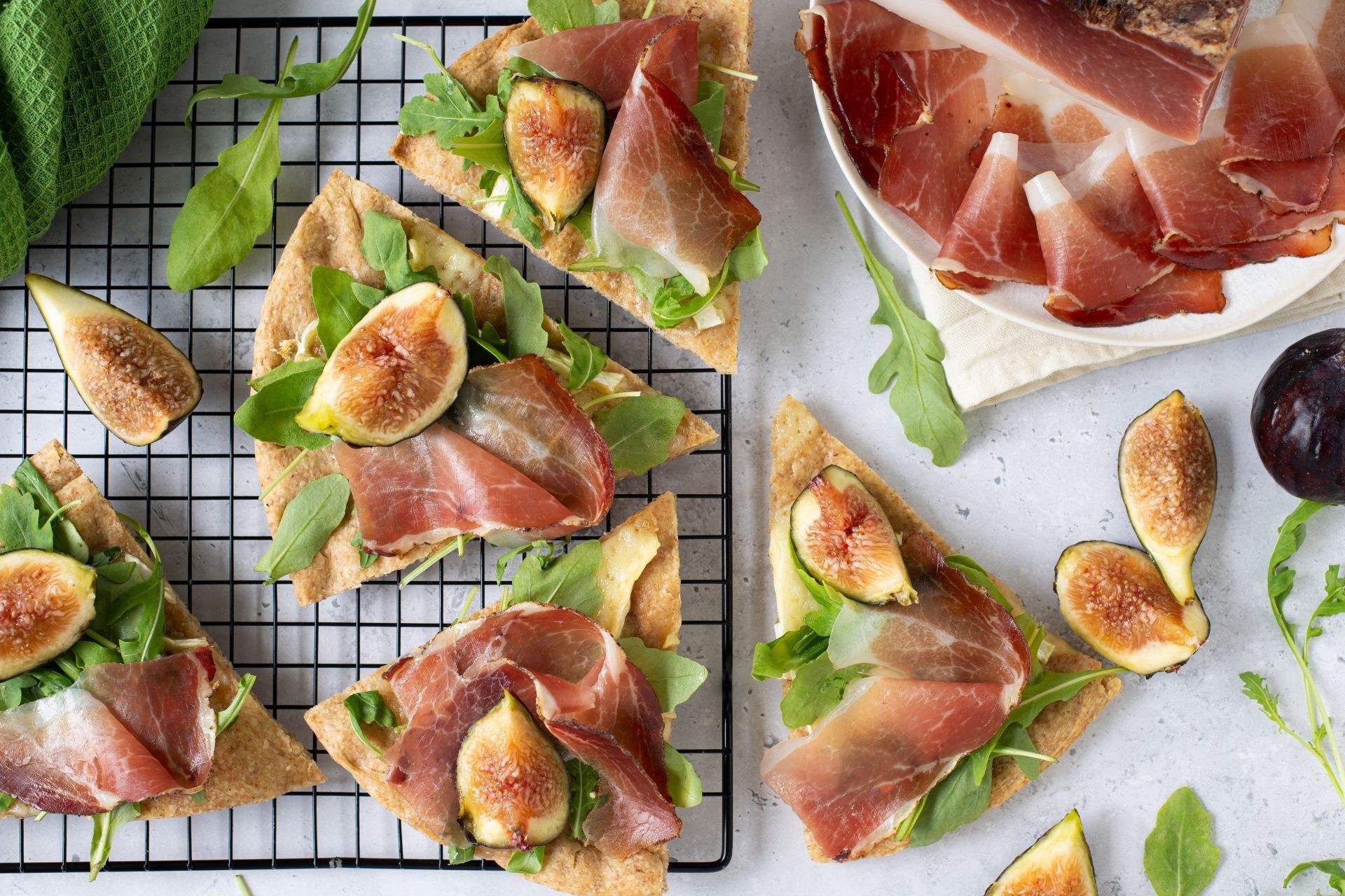 Vollkornfocaccia belegt mit Südtiroler Speck g.g.A., cremigem Brie, frischen Feigen und Rucola, in Stücke geschnitten serviert.