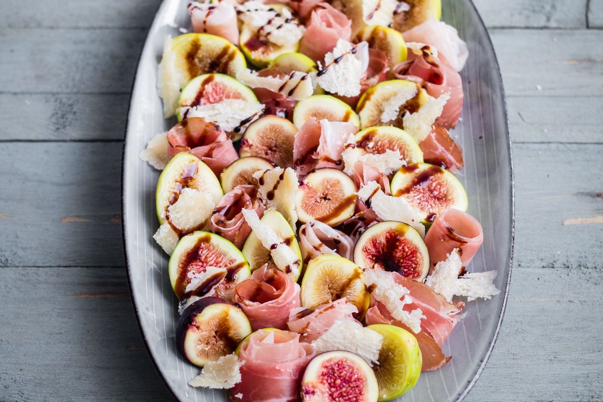 Feigensalat mit Südtiroler Speck g.g.A., gehobeltem Hartkäse und Balsamico-Creme, angerichtet auf frischem Salat.