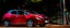 Red Nissan Leaf plugged in charging by a lamppost in a dimly lit car park
