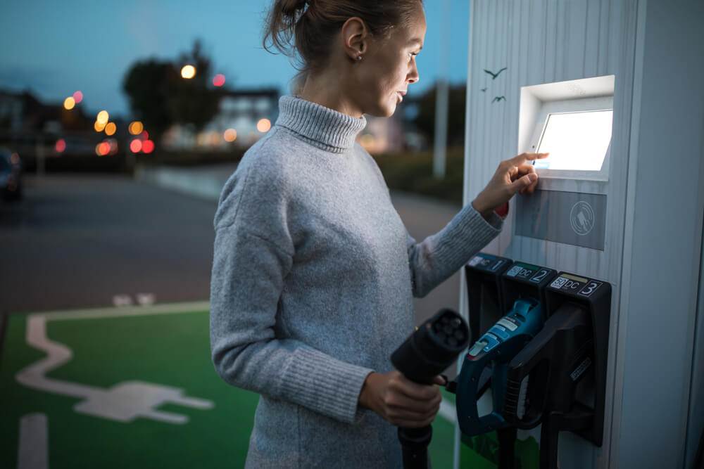 Woman holding an EV charging cable in one hand while she looks at payment screen