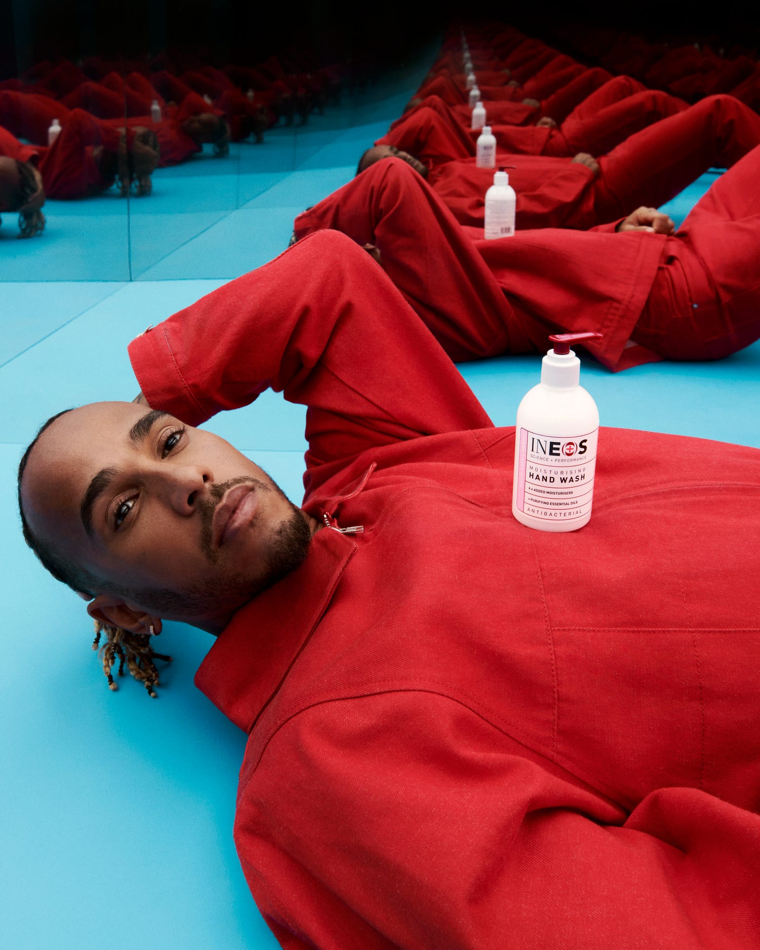 a photo of lewis hamilton in a red shirt holding some sanitiser in room of mirrors