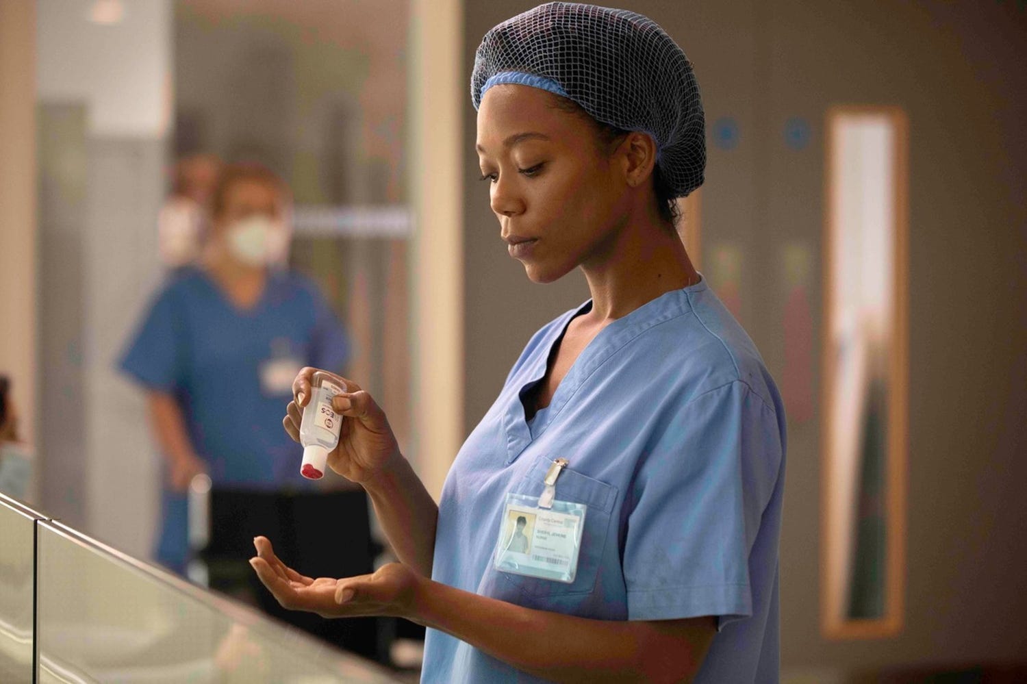 a woman in scrubs and a hair net applying ineos hygienics hand sanitiser