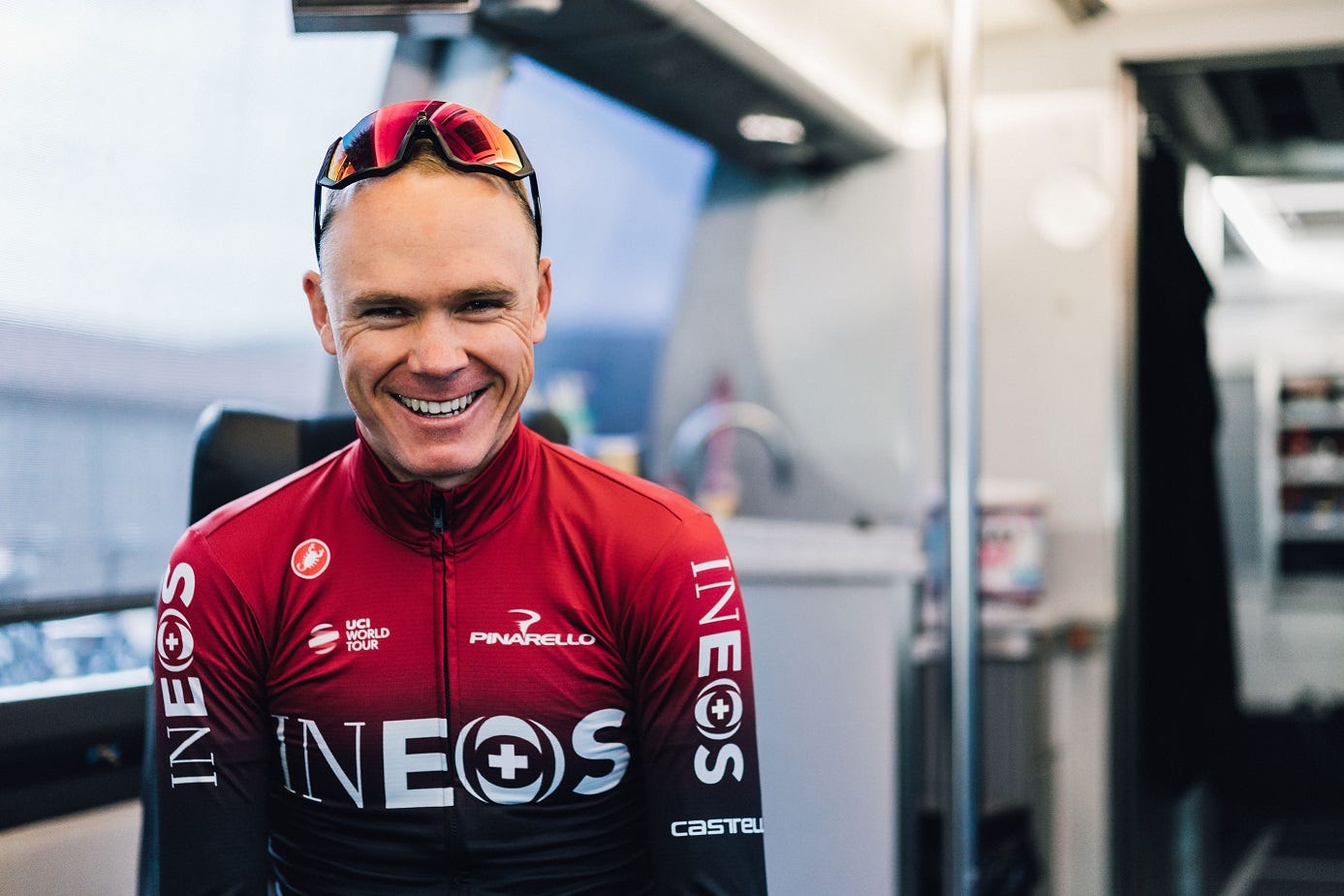 chris froome in a red ineos cycling kit smiling at the camera