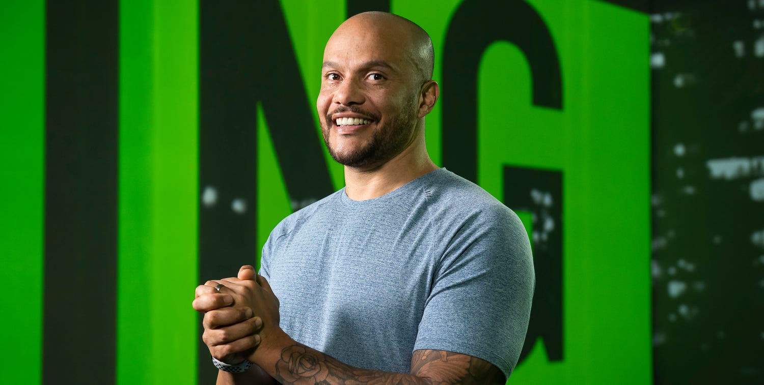 a photo of harry jameson in a grey shirt in a black and green room smiling at the camera