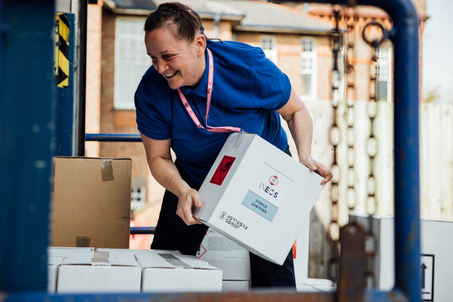 a woman in scrubs lifting a box of ineos hand sanitiser