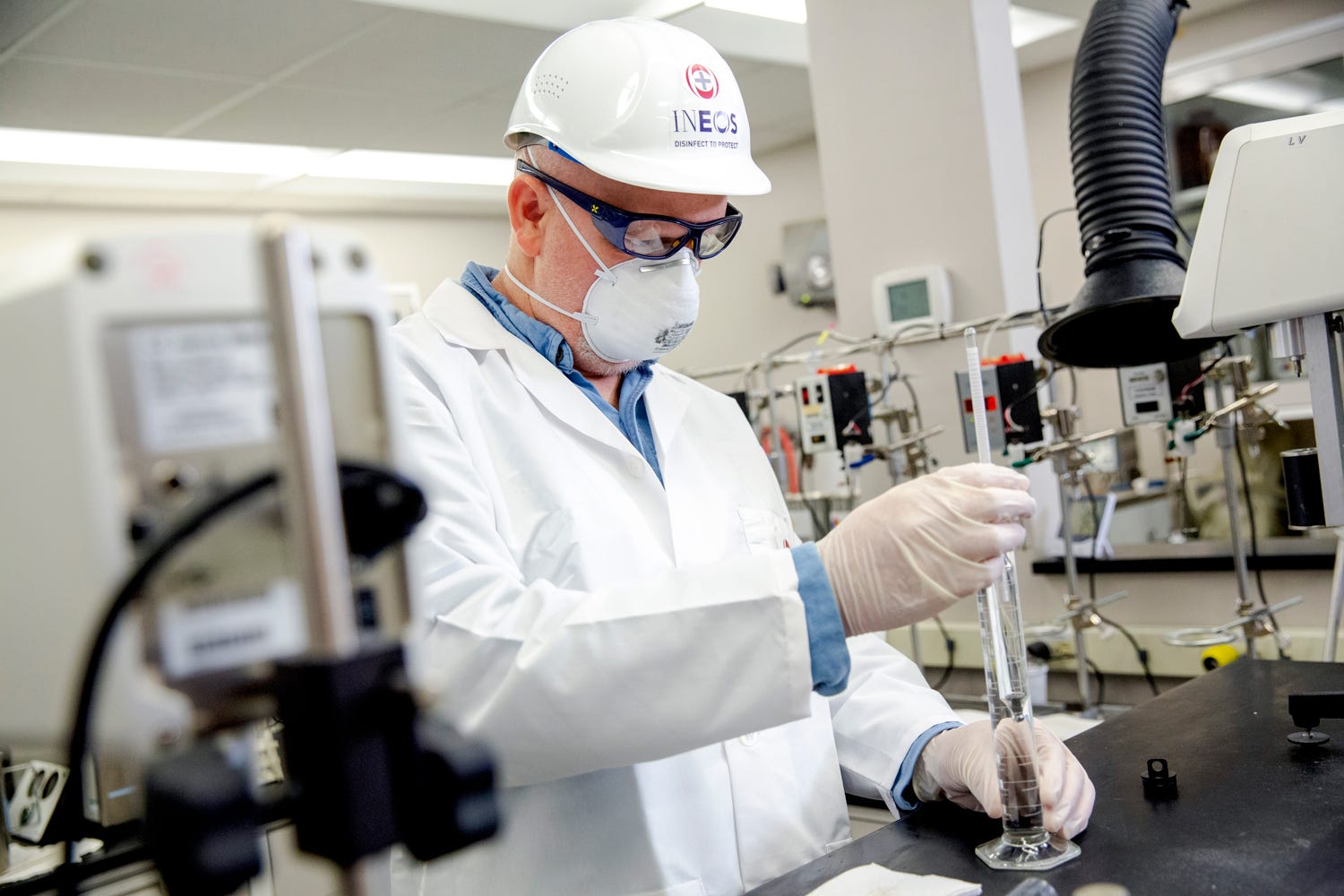 a man in a lab coat and hard hat working in an ineos lab
