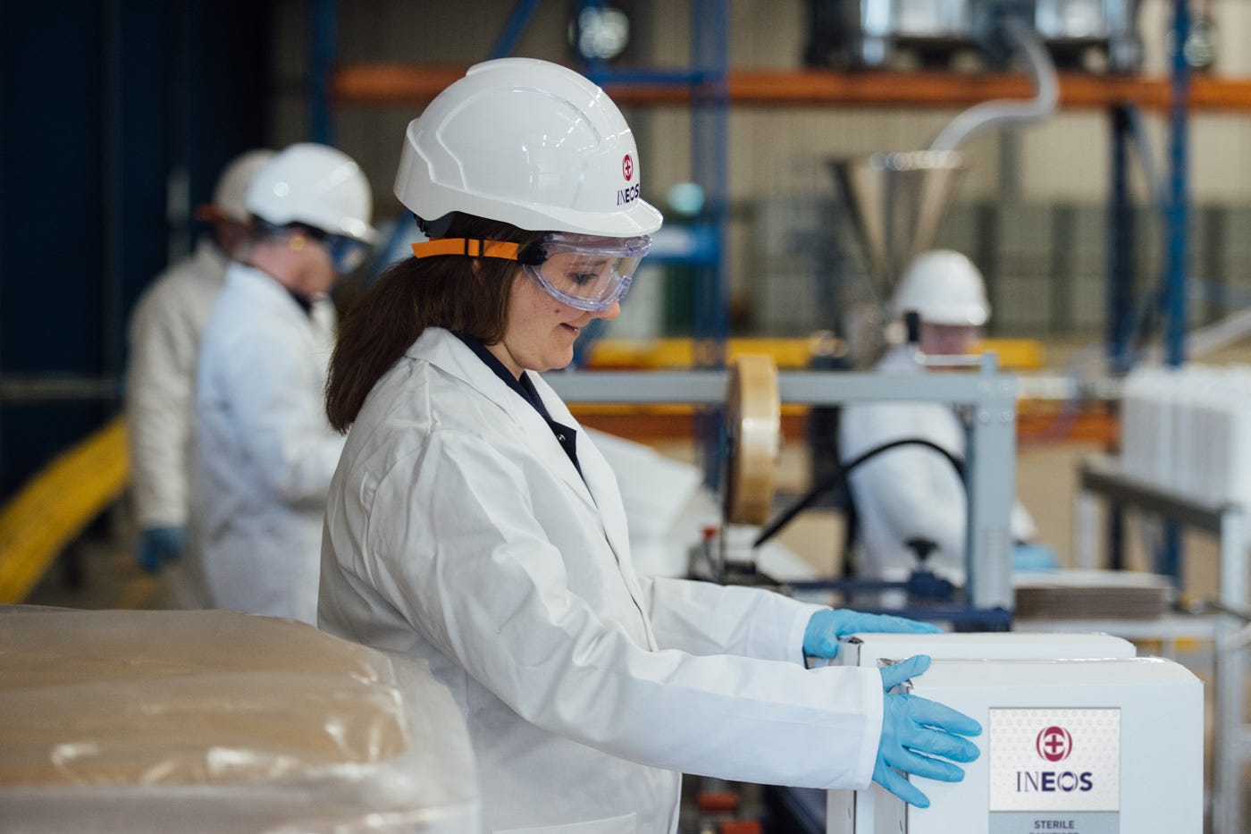 a woman wearing a lab coat and hard hat while working in an ineos hygienics factory