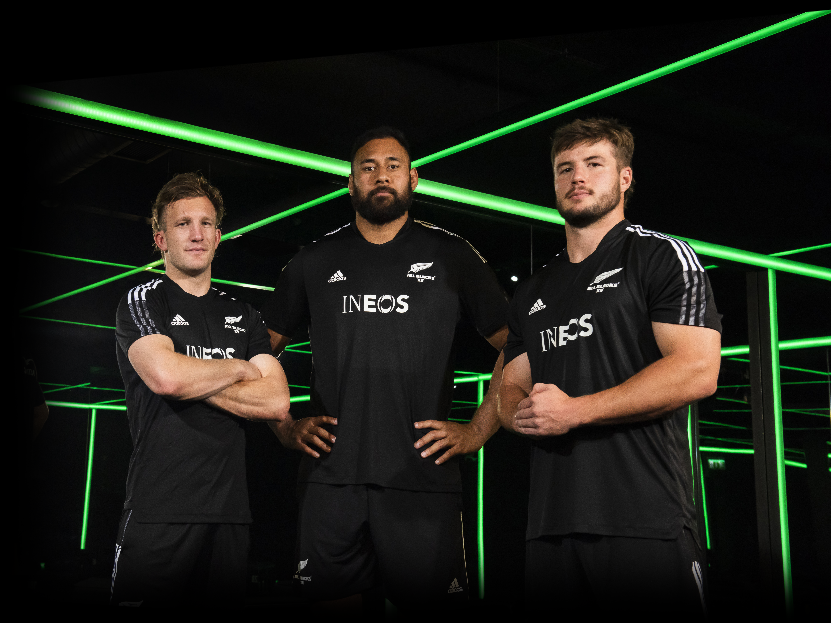 a photo of three all blacks looking down at the camera in black ineos all blacks shirts in a green and black room