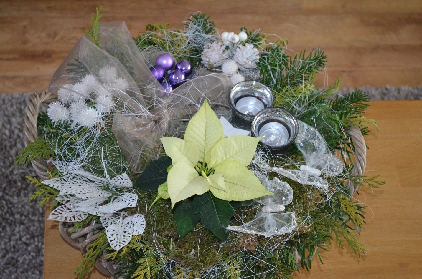 Een kerststukje in een mand voor op tafel met dennentakken, een kerstroos, kaarsjes en kerstversiering