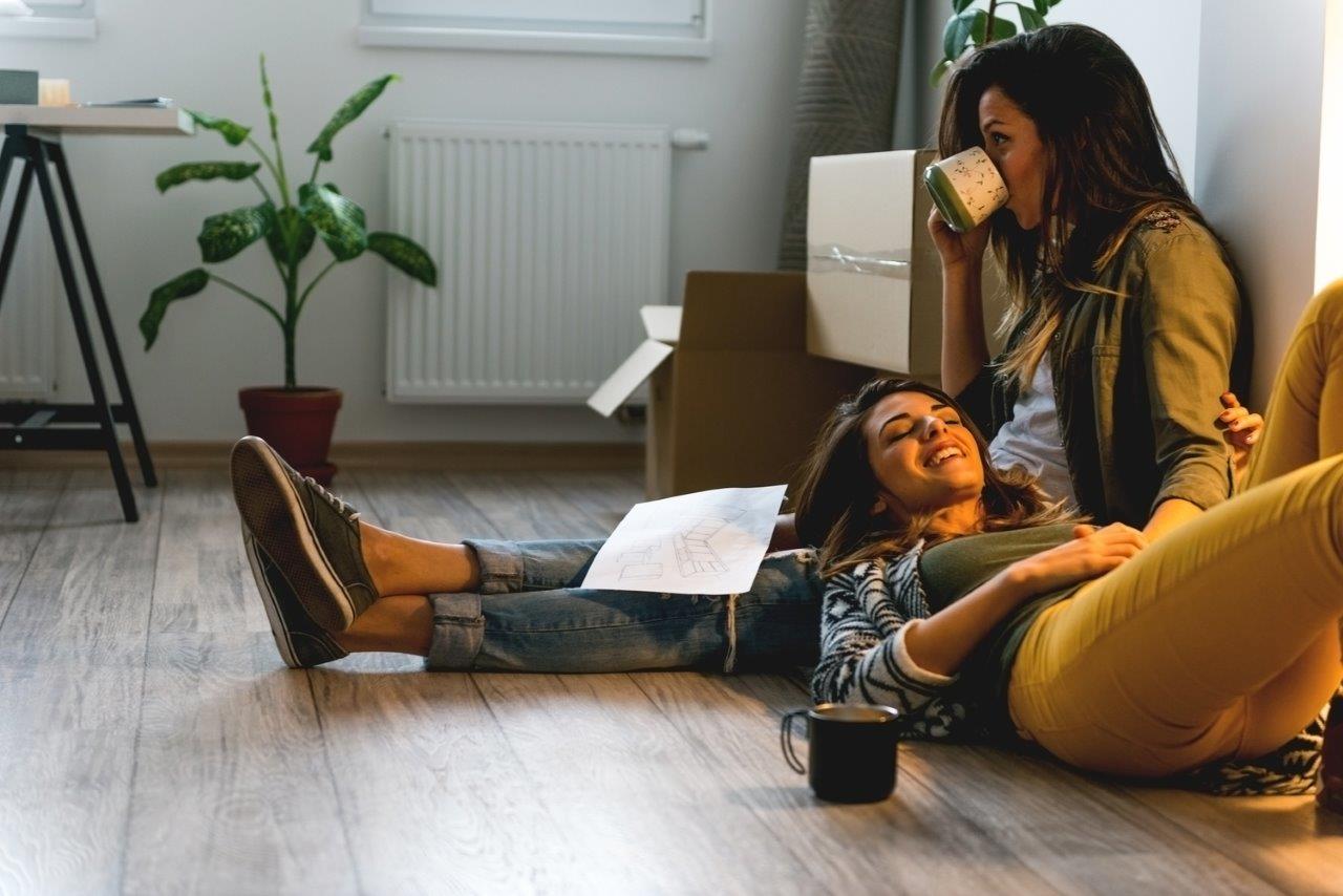 A couple take a break from unpacking to enjoy a hot drink whilst sitting on their living room floor