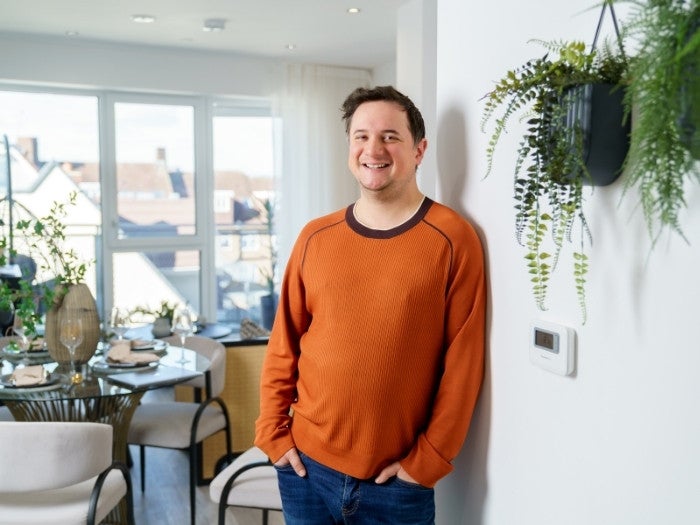 Matthew smiles as he poses for a photo with his open-plan dining and living area in the background.