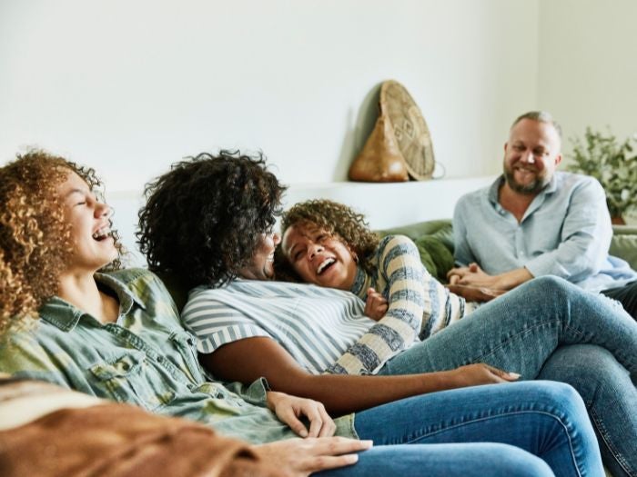 A family of 4 laugh together as they relax in their living room