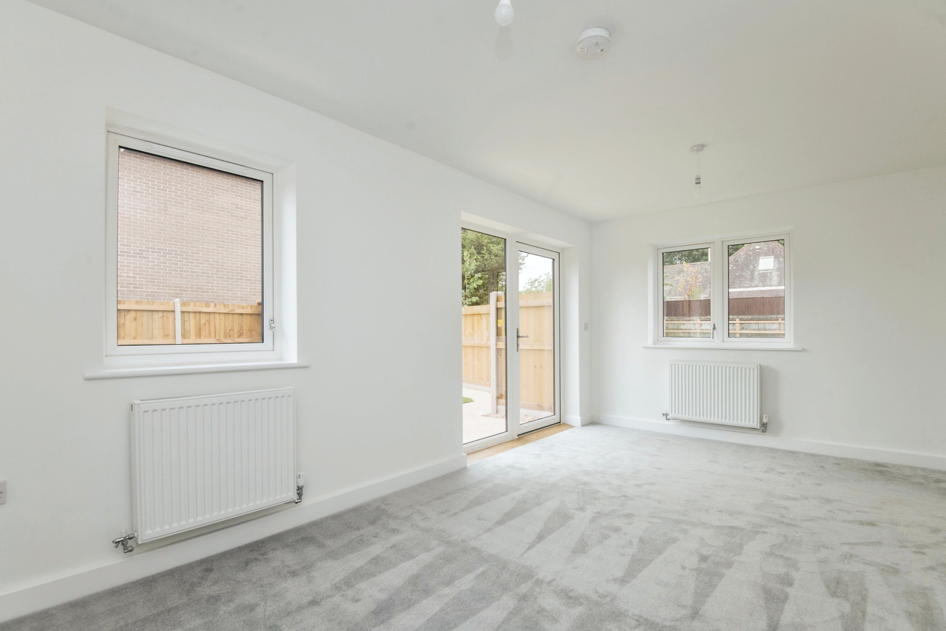 Living area, with grey carpet, two windows and patio doors