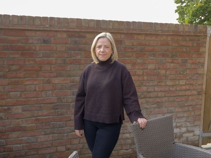 Lucy rests her hand on a garden chair as she stands in her garden