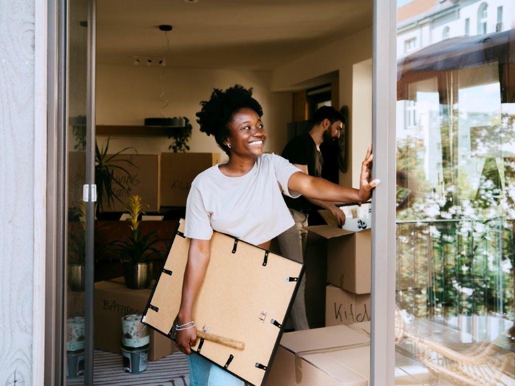 A lady moving into her new home, holding a picture frame and smiling