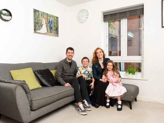 Max, Charlotte and two of their children pose for a photo on their sofa.