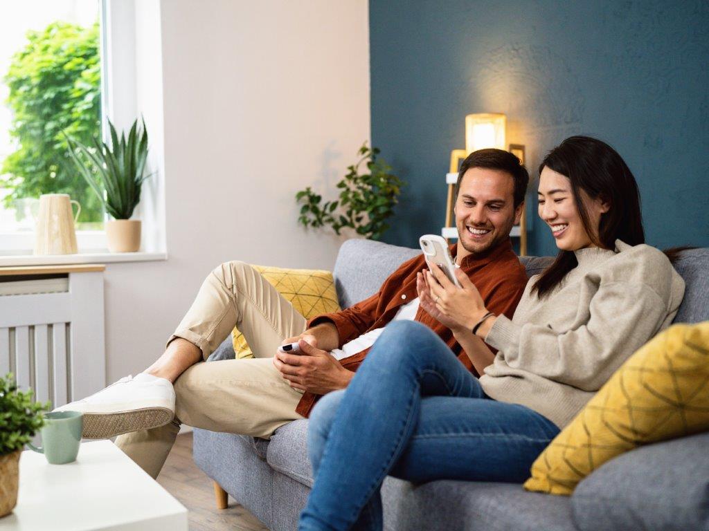 A couple sat on a sofa smiling, both looking at a phone the women is holding