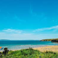 Colourful umbrella and chairs above a beach with cliffs, sea and blue sky