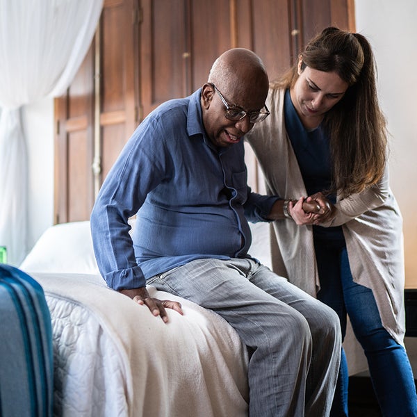 Een vrouw helpt een oudere man uit een bed.