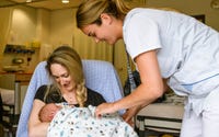 Moeder met een baby op schoot wordt geholpen door een verpleegkundige. 