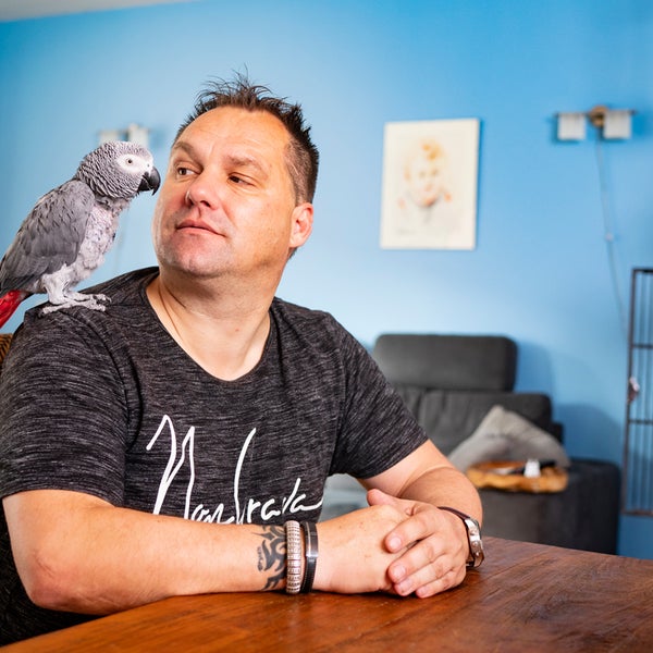 Manfred Roubos zit aan tafel met een papegaai op zijn schouder