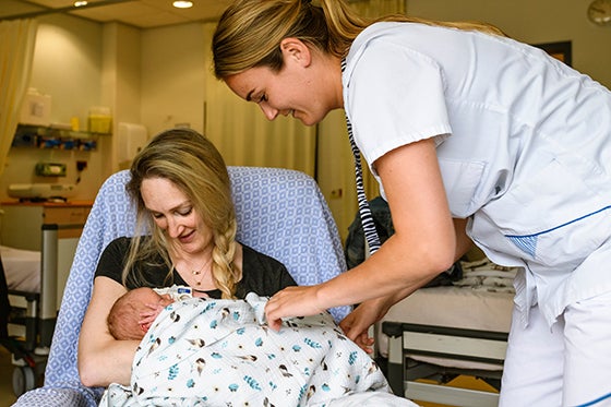 Een verpleegster in een witte uniform helpt een moeder die haar pasgeboren baby vasthoudt in een ziekenhuiskamer