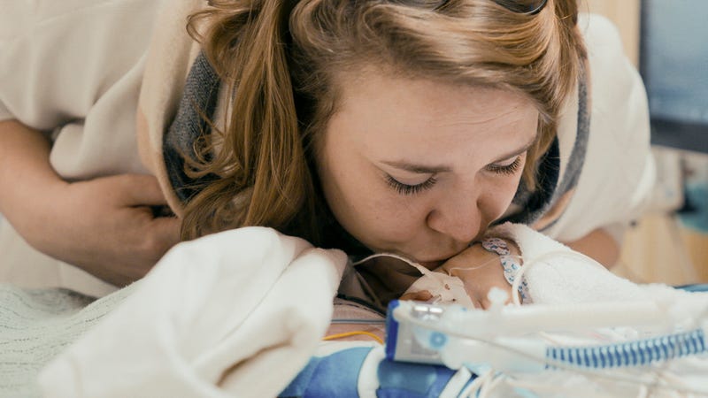 Een moeder kust haar baby, die aan de beademing in een ziekenhuisbedje ligt.