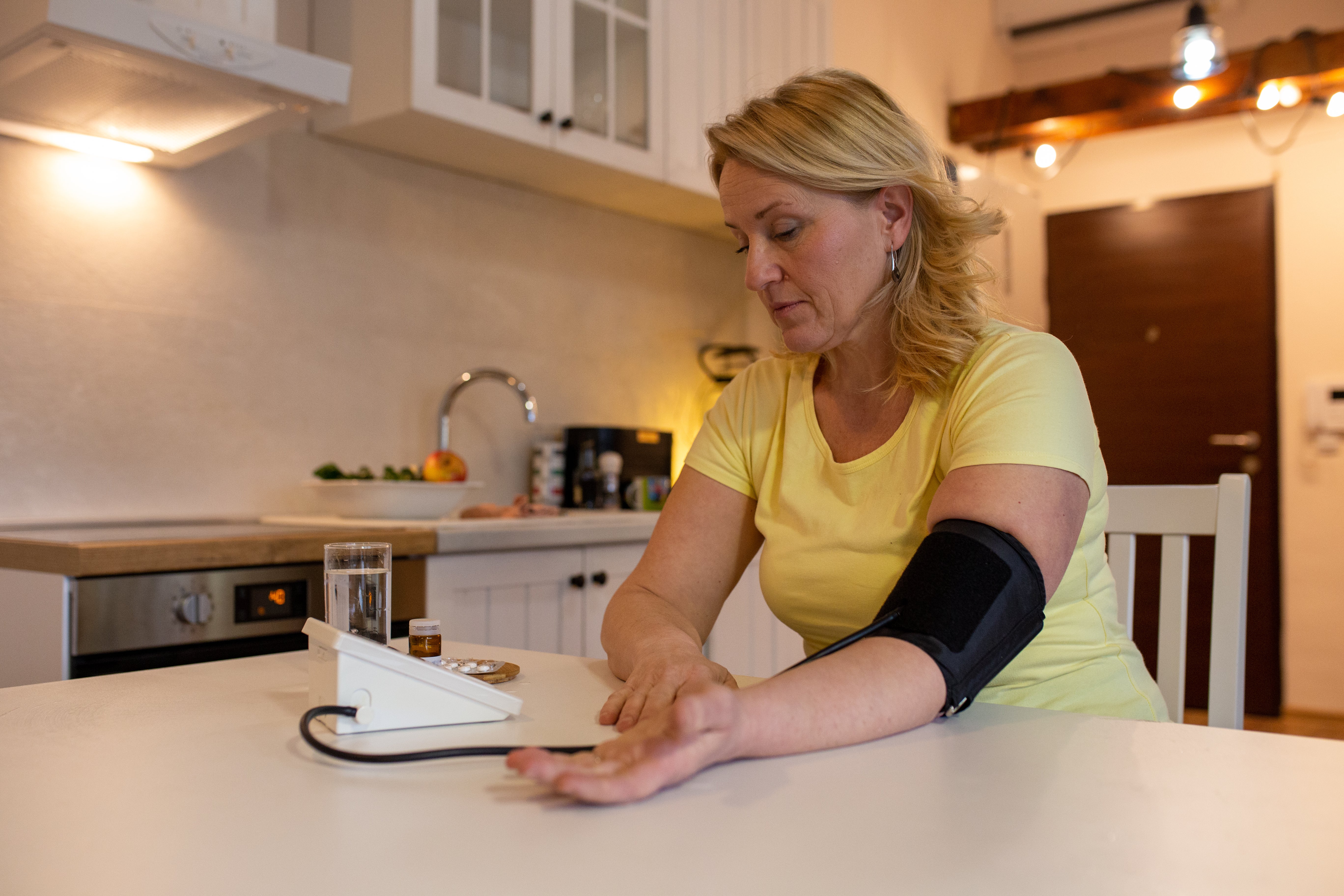 Vrouw aan de keukentafel meet haar eigen bloeddruk op.
