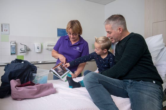 Voorbereiding op een operatie door de medisch pedagogisch zorgverlener. Vader en kind kijken naar de foto's en materialen