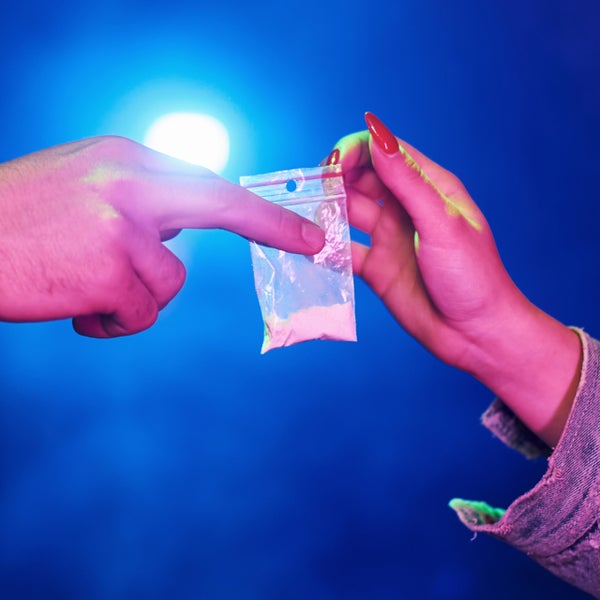 Twee handen wisselen een zakje met drugs in poedervorm uit.