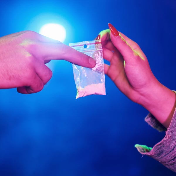 Twee handen wisselen een zakje met drugs in poedervorm uit.