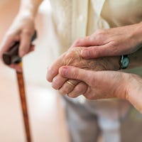 Een zorgverlener houdt de hand vast van een ouder persoon.