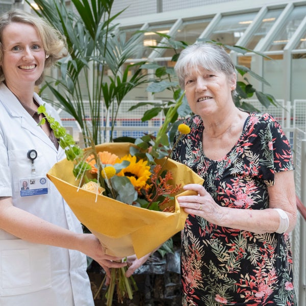 Een zorgverlener overhandigt een patiënt een boeket bloemen omdat de patiënt de 600e longtransplantatie heeft ondergaan.