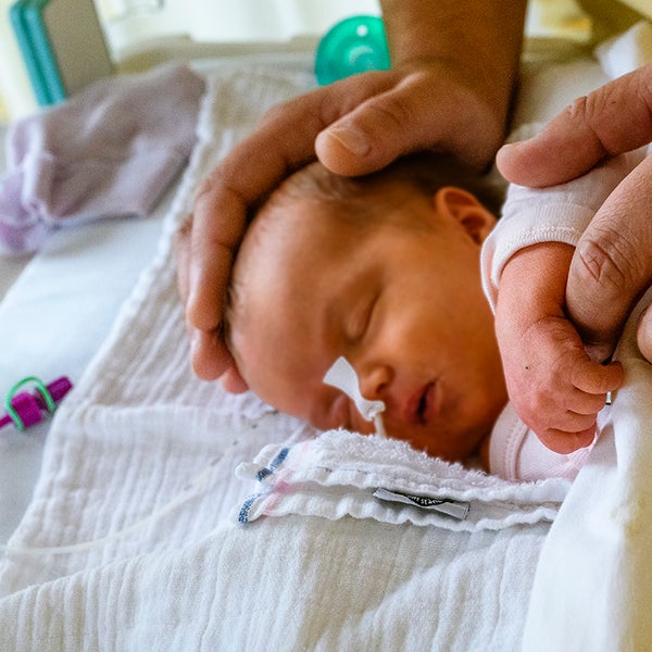 Verzorgende legt handen op een baby in een bedje