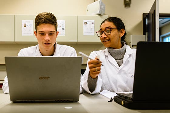 Twee studenten in laboratoriumjassen werken samen aan laptops in een laboratorium
