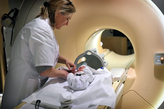 Baby ligt op MRI-tafel om zo een MRI te laten maken. Zorgverlener treft de laatste voorbereidingen bij de baby.