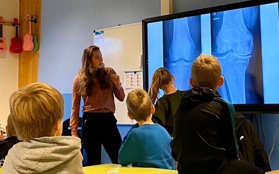 Een vrouw voor een groot scherm legt kinderen een röntgenfoto uit