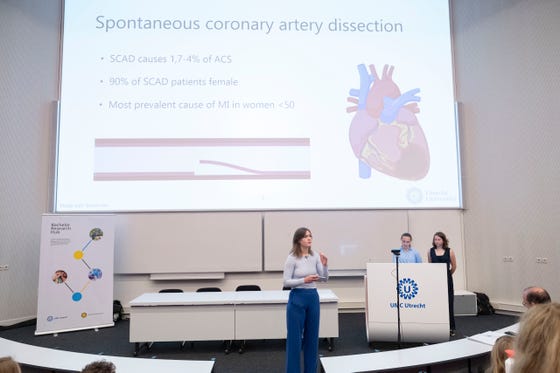 Studenten presenteren hun onderzoek in de Vrouwenhart Challenge. Op het scherm staat "Spontanenous coronary artery dissection" met een getekende afbeelding van een anatomisch hart.