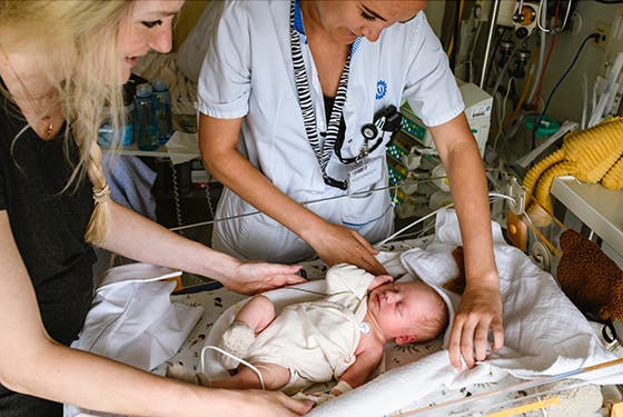 Een verpleegster en een moeder verzorgen een baby op de intensive care UMC Utrecht, omringd door medische apparatuur
